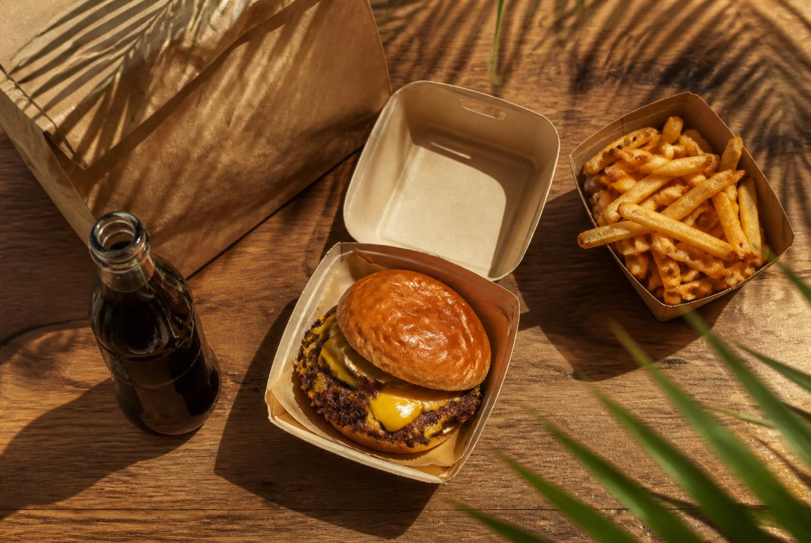 Pedido de hamburguesa a domicilio en Cancún: smash burger en caja, papas y bebida sobre mesa de madera
